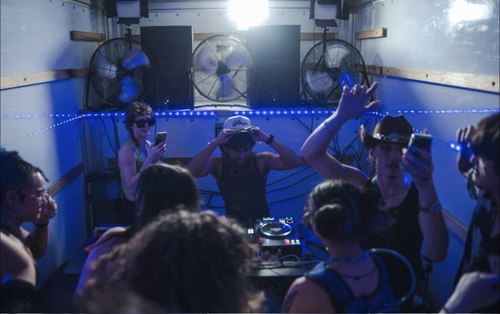 The DJ adjusting his cap under a white key light in the truck, hands in the air around him